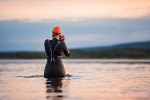 A man in a wetsuit standing in the water at sunset.