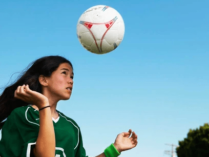 A woman in a green jersey with a football ball in the air.