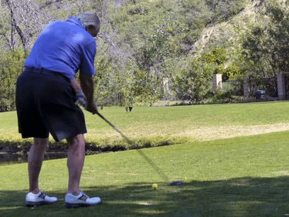An older man hitting a golf ball on a golf course.
