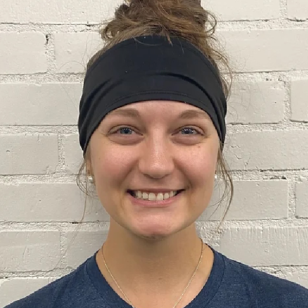 A young woman wearing a headband in front of a brick wall.