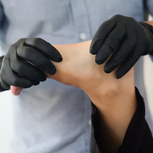 A man in black gloves is putting black gloves on his foot.