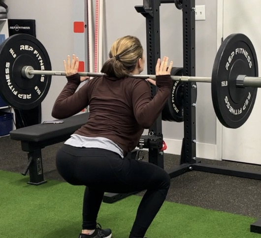 A woman squatting with a barbell in a gym.