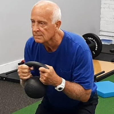 An older man squatting with a kettlebell in a gym.
