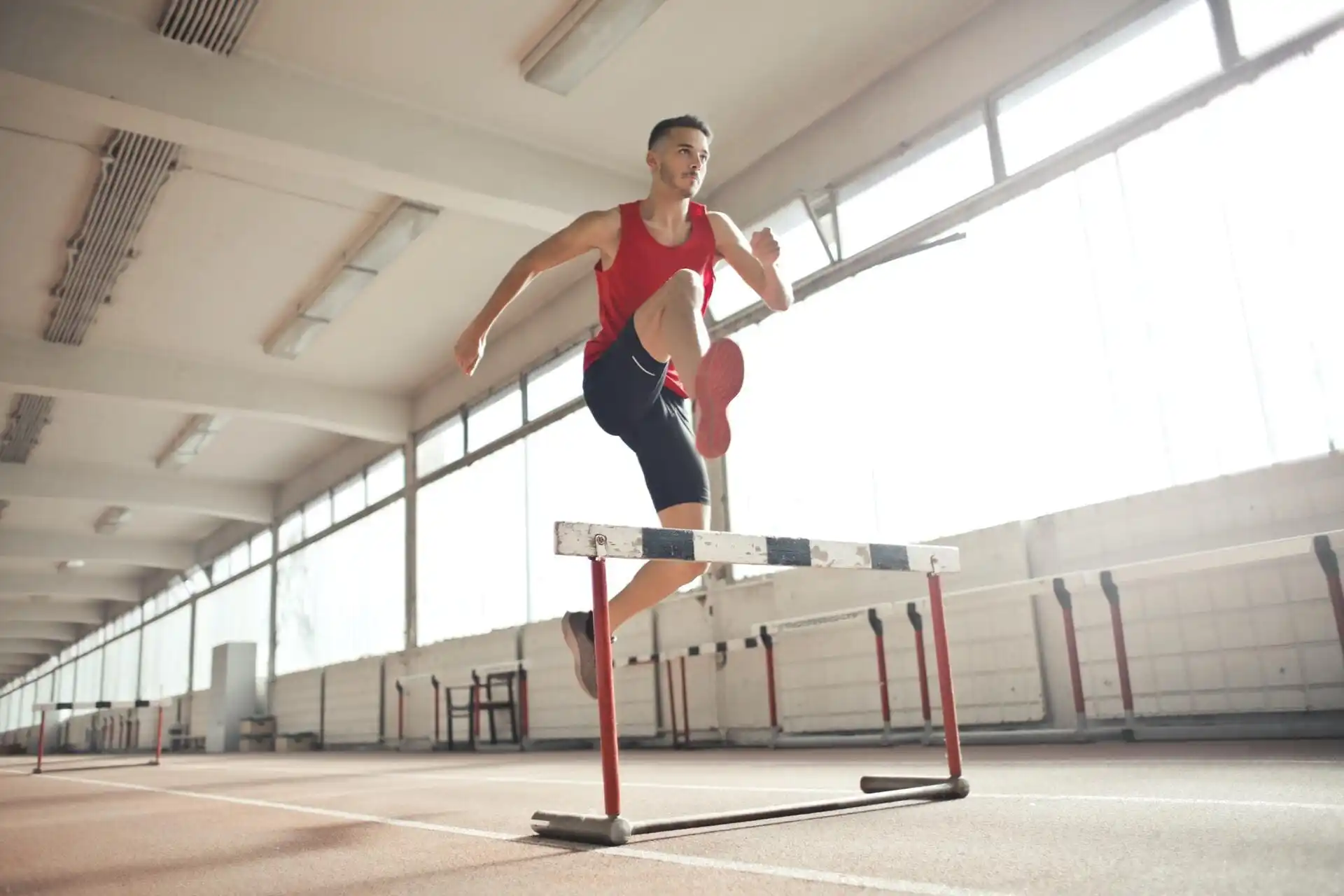 A man jumping over a hurdle in an indoor track.