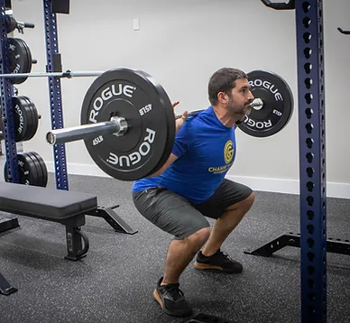 A man squatting with a barbell in a gym.