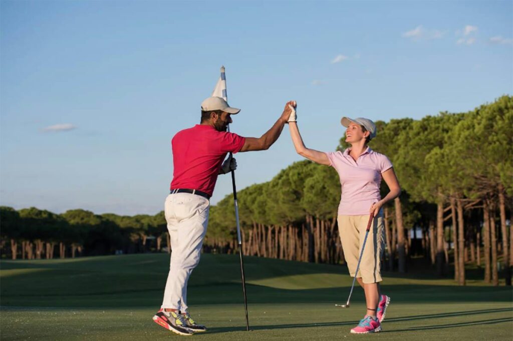 A man and woman high fiving each other on a golf course.