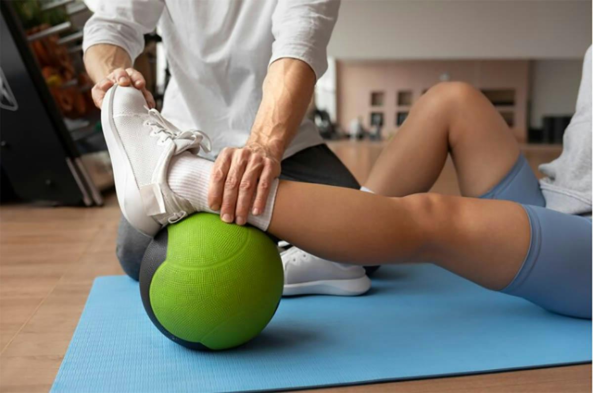 A woman is putting her foot on a green exercise ball.