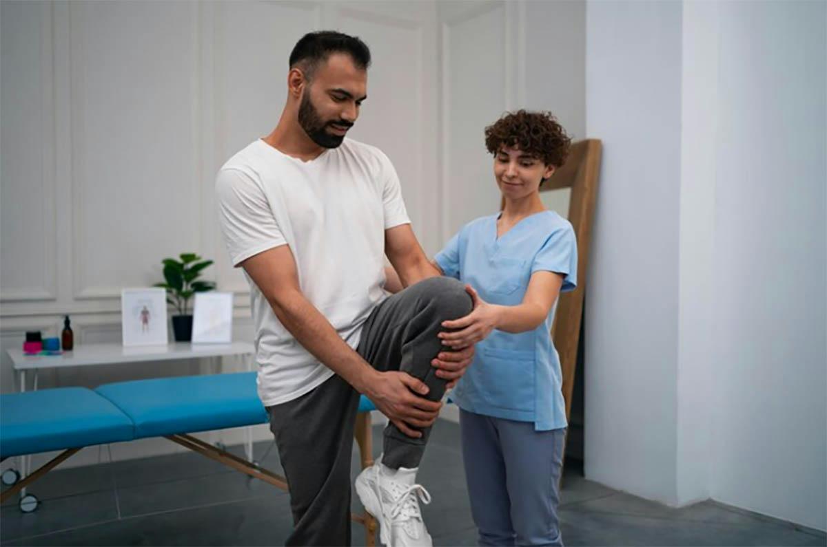 A male physiotherapist is helping a patient with a knee injury.